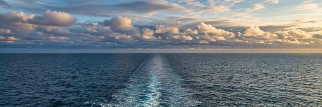 A boat's wake trailing toward an empty horizon on open ocean, at least three nautical miles from land