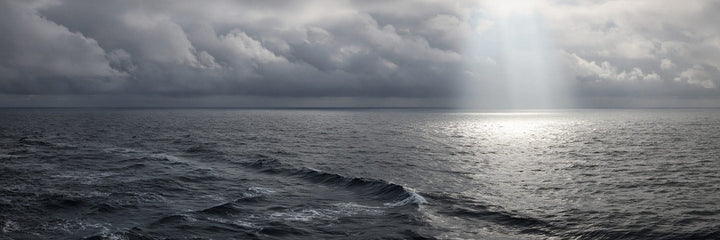 Overcast open ocean with a shaft of sunlight breaking through cloud onto the water