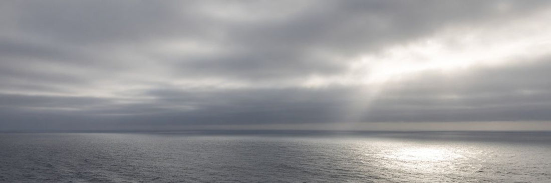 Open Atlantic swells under an overcast sky with sunlight breaking through, the kind of ocean water beyond the three-nautical-mile line where a burial at sea is federally permitted
