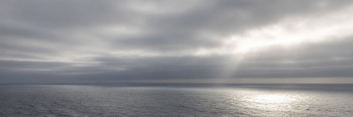Open Atlantic swells under an overcast sky with sunlight breaking through, the kind of ocean water beyond the three-nautical-mile line where a burial at sea is federally permitted