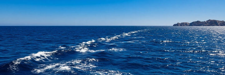 Open ocean swell under a clear sky more than three nautical miles offshore, the setting where a biodegradable sea burial urn is released